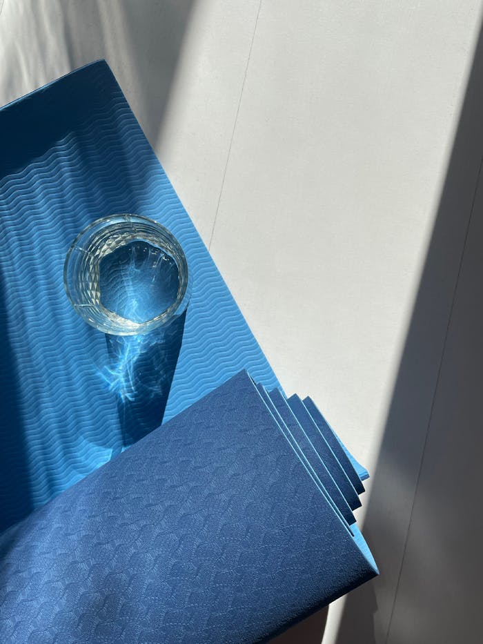 A blue yoga mat with a glass reflecting sunlight, creating a calm and relaxed ambiance.